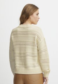 Maglione color crema con design a righe in maglia aperta, polsini e orlo a coste. Caratterizzato da un colletto rotondo e una vestibilità comoda.