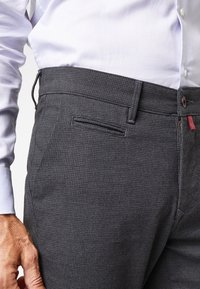 Pantaloni grigi a fantasia con una finitura testurizzata, dotati di tasca anteriore, passanti per cintura e un'etichetta del marchio discreta. Camicia di colore chiaro in contrasto.