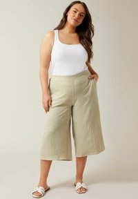 Lichtgroene, wijdvallende broek gemaakt van textiel met structuur. Kenmerkt zich door een comfortabele elastische tailleband en zijzakken. Gepaarde met een witte tanktop en sandalen.
