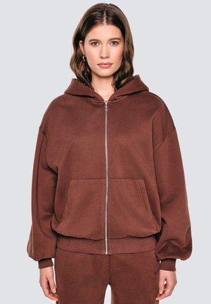 Pruun zip-up kapuutsiga dressipluus, mis on valmistatud pehmest kangast, sisaldab kapuutsi, esipokke ja soonikuga varrukaid. Lihtne disain, ilma nähtavate mustrite või aktsentideta.