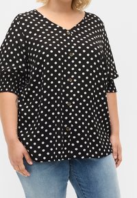 Svart blus med polka prickar, v-ringning, korta puffärmar och knäppning, med vita prickar och en avslappnad passform.