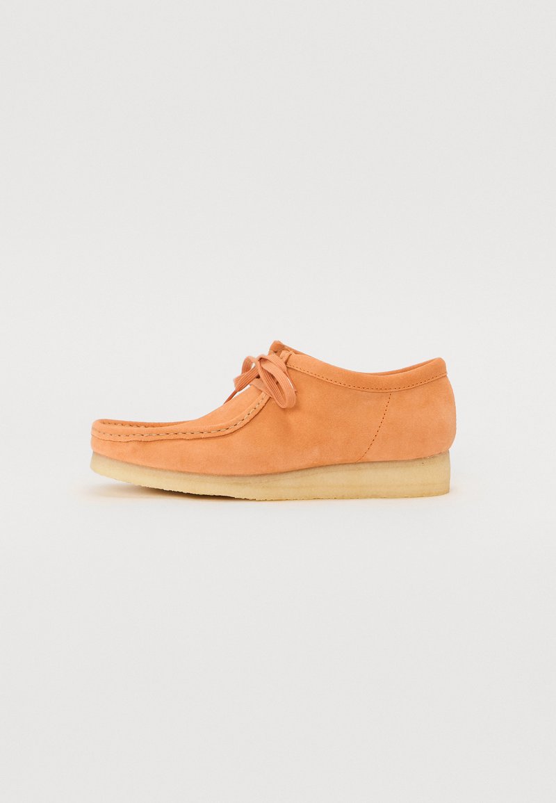 Orange suede shoe with a rounded toe, leather lacing detail, and a flat rubber sole, featuring a simple, clean design.