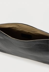 Fekete, texturált bőrtok bézs színű textil belsővel és nyitott ezüst cipzárral, fehér háttéren.