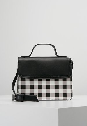 Czarna i biała torebka w kratę z czarną klapką, górnym uchwytem oraz odpinanym paskiem na ramię, umieszczona na białej powierzchni.