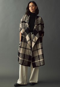 Overdimensioneret cardigan med ternet mønster i en beige og sort uldblanding, med åben front og rullede ærmer, parret med crèmefarvede bredbenede bukser.
