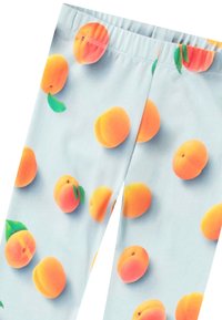 Leggings en tissu léger présentant un fond bleu pastel avec un motif répété d'illustrations réalistes de pêches.