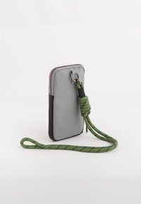 Pochette pour téléphone en tissu gris avec un fond noir, dotée d'une sangle tressée verte et de matériel en argent. De forme rectangulaire, avec fermeture zippée.