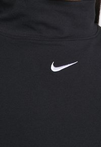 Svart rullkrage topp i ribbat tyg med en liten vit Nike-logga på vänster sida. Slät textur. Närbild.