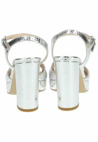 Sandales argentées à talons avec un motif en peau de serpent, dos ouvert, bracelet au niveau de la cheville avec boucle et épais talon carré. Texture lisse, finition brillante.