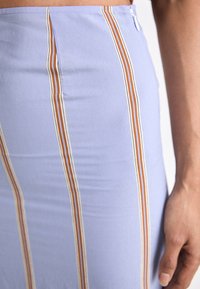 Hemelsblauwe rok met verticale strepen in oranje en wit, voorzien van een zijsplit en een gladde textuur. Gemaakt van een rekbare stof.