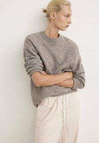 Grijze, gebreide trui met een ronde hals en opgerolde mouwen, gecombineerd met lichtgestreepte broek met een losse pasvorm en een elastische tailleband.