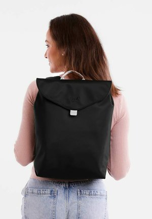 Black backpack made of fabric, featuring a fold-over flap, a subtle logo, and adjustable straps. Smooth texture with minimalistic design.