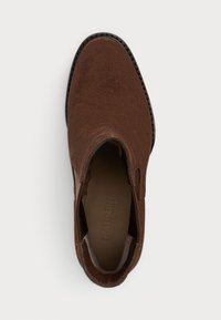 Chaussure slip-on en daim marron avec un bout arrondi et des panneaux latéraux élastiques. Tige texturée et doublure intérieure lisse. Détail de couture noire.