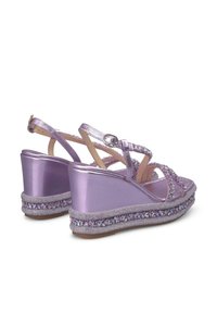 Les sandales compensées métalliques violettes présentent un design de bride ornée de bijoux et une semelle texturée, avec une base large et des brides de cheville réglables.