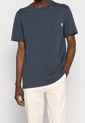 Marineblaue Kurzarm-T-Shirt aus glattem Stoff. Verfügt über eine Brusttasche und einen abgerundeten Halsausschnitt. Wird mit hellen Hosen getragen.