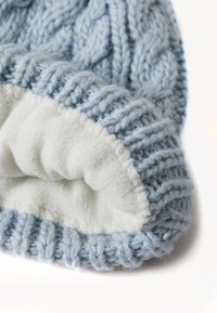 Cappello lavorato a maglia di colore azzurro chiaro con un motivo a treccia testurizzato, dotato di una morbida fodera in pile bianco lungo il bordo interno.