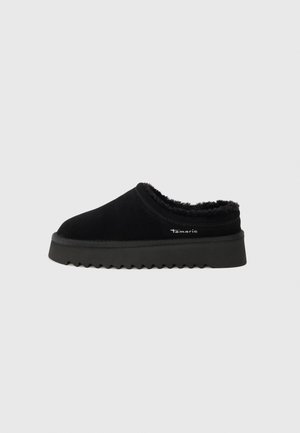Chaussure noire à enfiler en suède, dotée d'une doublure en fourrure douce. Présente une épaisse semelle en caoutchouc texturé avec un motif en zigzag. Marque Tamars visible.