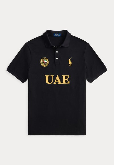 Μαύρο πόλο με κίτρινο κείμενο UAE, έμβλημα UAE στο αριστερό στήθος και κίτρινο λογότυπο παίκτη πόλο Ralph Lauren στο δεξί στήθος.