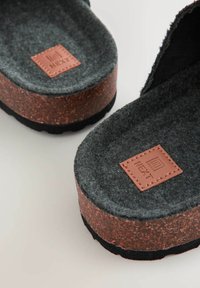 Graue rutschfeste Slidesandalen mit einer braunen Korksohle, ausgestattet mit einem genähten Lederetikett, das mit "NEXT" geprägt ist. Das Design weist eine strukturierte Oberfläche auf.