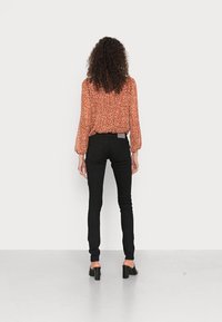 Blusa floral vermelha com mangas balão, combinada com jeans ajustados pretos e sapatos de salto bloco pretos. Modelo visto de costas.