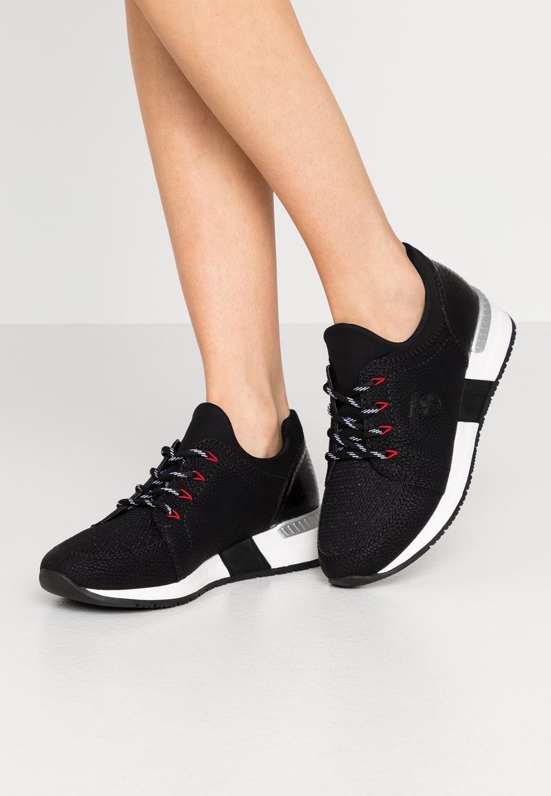 Chaussures de sport noires avec une tige en tissu texturé, lacets rouges et blancs, une semelle intermédiaire blanche et une semelle extérieure en caoutchouc noire.