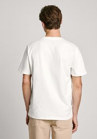 Camiseta de algodón blanca con cuello redondo y mangas cortas, presentada por la parte de atrás. Diseño sencillo sin logotipos ni patrones visibles.