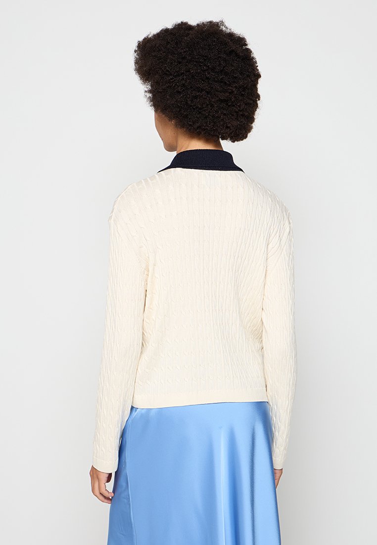 Maglione a trecce color crema con colletto blu navy, caratterizzato da un motivo testurizzato e maniche lunghe, visto da dietro.