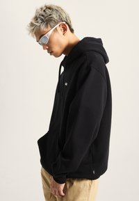 Felpa nera con cappuccio realizzata in tessuto morbido, dotata di tasca a marsupio, cappuccio con lacci e un piccolo logo sul petto.