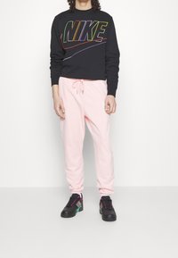 Czarna bluza z długim rękawem z wielokolorowym logo "NIKE", połączona z jasnoróżowymi spodniami dresowymi z elastycznym pasem. Czarno-turkusowe sneakersy.