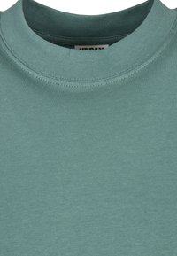 Gros plan d'un t-shirt vert sarcelle à col rond montrant l'encolure et la texture du tissu.