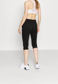 Svarta capri leggings med en åtsittande design, mjuk textur och anklar, tillsammans med en vit träningströja och vita sneakers.