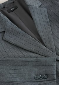 Blazer a rayas grises con forro liso, que presenta tres botones negros en los puños y un diseño moderno y ajustado.