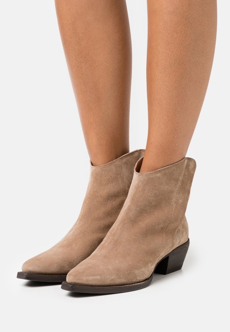 Botas de tobillo de ante en beige claro, con punta afilada y un tacón bajo en bloque. Diseño sencillo con textura suave y un pequeño corte en los tobillos.