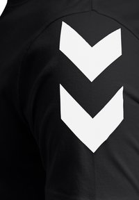 Zwei weiße, nach unten zeigende Chevron-Muster, auf den schwarzen Stoffärmel eines Kleidungsstücks gedruckt.