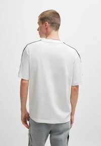 Weißes Kurzarm-T-Shirt mit lockerer Passform, mit schwarzen Seitenstreifen an den Schultern. Hergestellt aus einem glatten, leichten Stoff.