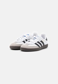 White athletic shoes with black stripes, grey suede toe, and textured rubber sole. Features blue accents and lace-up design.