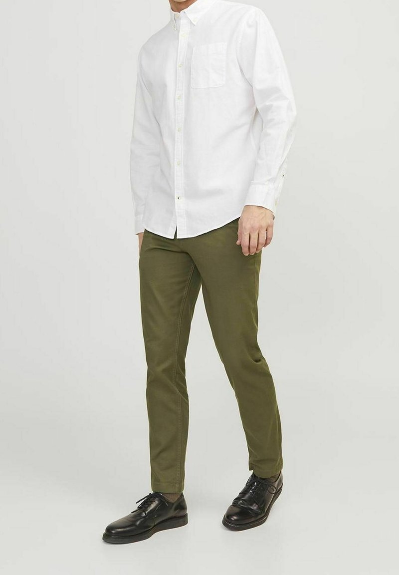 White long-sleeve button-up shirt with a chest pocket, paired with olive green slim-fit pants and black dress shoes. Smooth fabric, tailored fit.