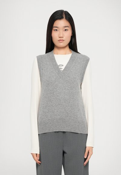 Gray knitted vest with a v-neck design, ribbed edges, and soft texture, worn over a long-sleeve cream shirt. Model stands front-facing.
