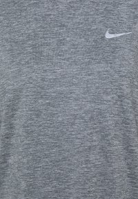 Harmaa urheilupaita, jossa on teksturoitu kangas ja pieni valkoinen Nike-logo vasemmassa yläkulmassa. Klassinen pyöreä kaula-aukko.