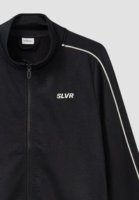 Zwarte zip-up jack met een hoge kraag, witte piping langs de schouders en een klein "SLVR" logo op de linkerkant van de borst.