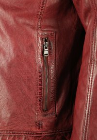 Rote Lederjacke mit strukturiertem Finish, schlankem Design und einer schrägen Reißverschlusstasche mit Metallbeschlägen an der Seite.