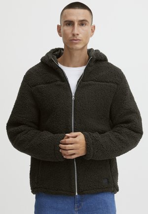 Dunkelgrüne, mit Fleece gefütterte Kapuzenjacke mit Reißverschluss, oversized Passform und zwei seitlichen Taschen. Verfügt über ein dezentes Logo-Patch an der unteren Seite.