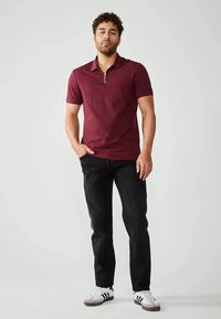 Polo de fecho em bordeaux com mangas curtas, combinado com jeans pretos e sapatilhas brancas com riscas pretas. Design simples e ajustado.