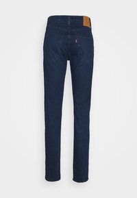 Mörkblå denimjeans sedda bakifrån med två fickor, bältesöglor och en brun läderlogotyp på midjan.