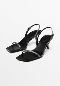 Tacchi slingback aperti neri con punta quadrata, cinturini metallici testurizzati e tacco a blocco modesto. Soletta e materiale esterno in pelle nera liscia.