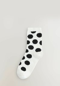 Białe skarpetki z dużymi czarnymi kropkami. Wykonane z miękkiego materiału z prążkowanym mankietem i gładką teksturą. Standardowy krój sięgający kostki.