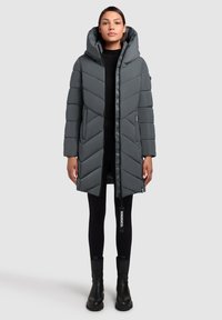 Grå dunjakke med et chevronmønster, lynlåslukning og en stor hætte. Har sidelommer og et mærketag på lynlåsen.