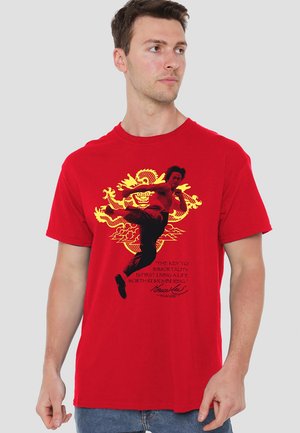 Rotes Baumwoll-T-Shirt mit einem bedruckten Design eines Kampfkünstlers in Schwarz und einem goldenen Drachen, mit inspirierendem Text darunter.