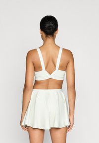 Světle zelený sportovní top s širokými ramínky a výstřihem do V, kombinovaný s ladící rozšířenou sukní. Hladký texture, minimalistický design.