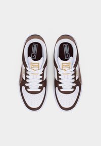 Ζευγάρι λευκά και καφέ αθλητικά παπούτσια Puma με άσπρα κορδόνια, κίτρινο λογότυπο Puma στη γλώσσα και πλευρά, σε λευκό φόντο, από πάνω.